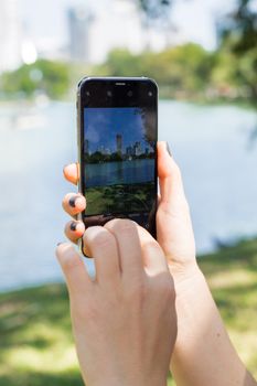 A person photographing a city skyline using a smartphone at a lakeside park.