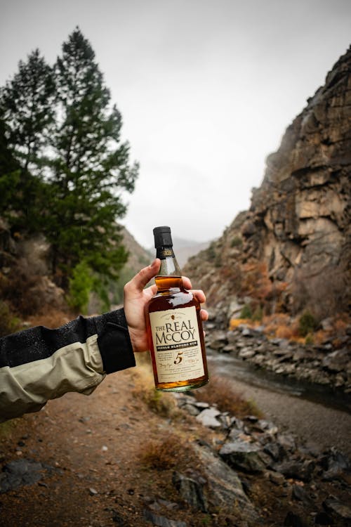 A person holding a bottle of whiskey in front of a mountain