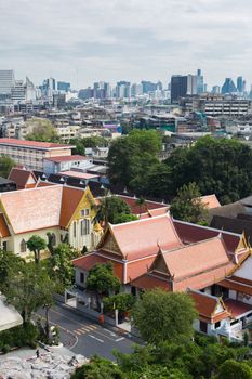 Aerial shot of Bangkok cityscape with traditional temples and modern buildings in daylight.