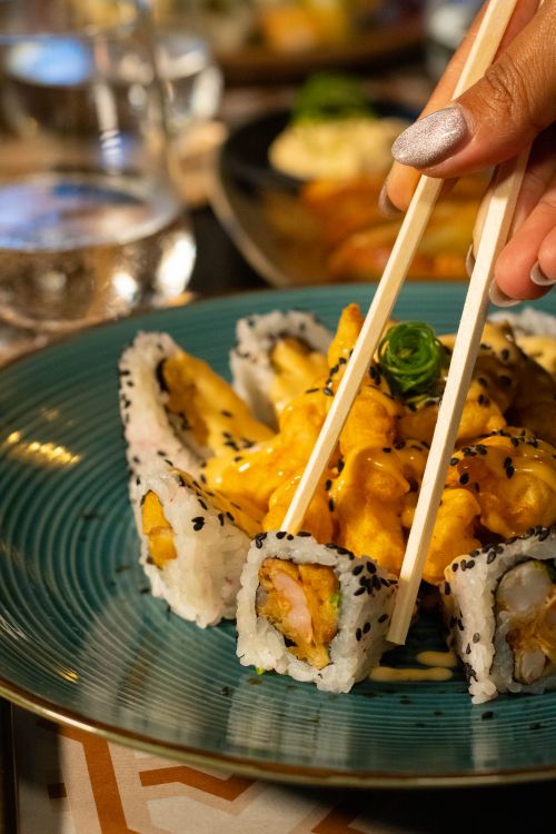 Free Close-up of a hand holding chopsticks with sushi roll, highlighting deliciousness. Stock Photo