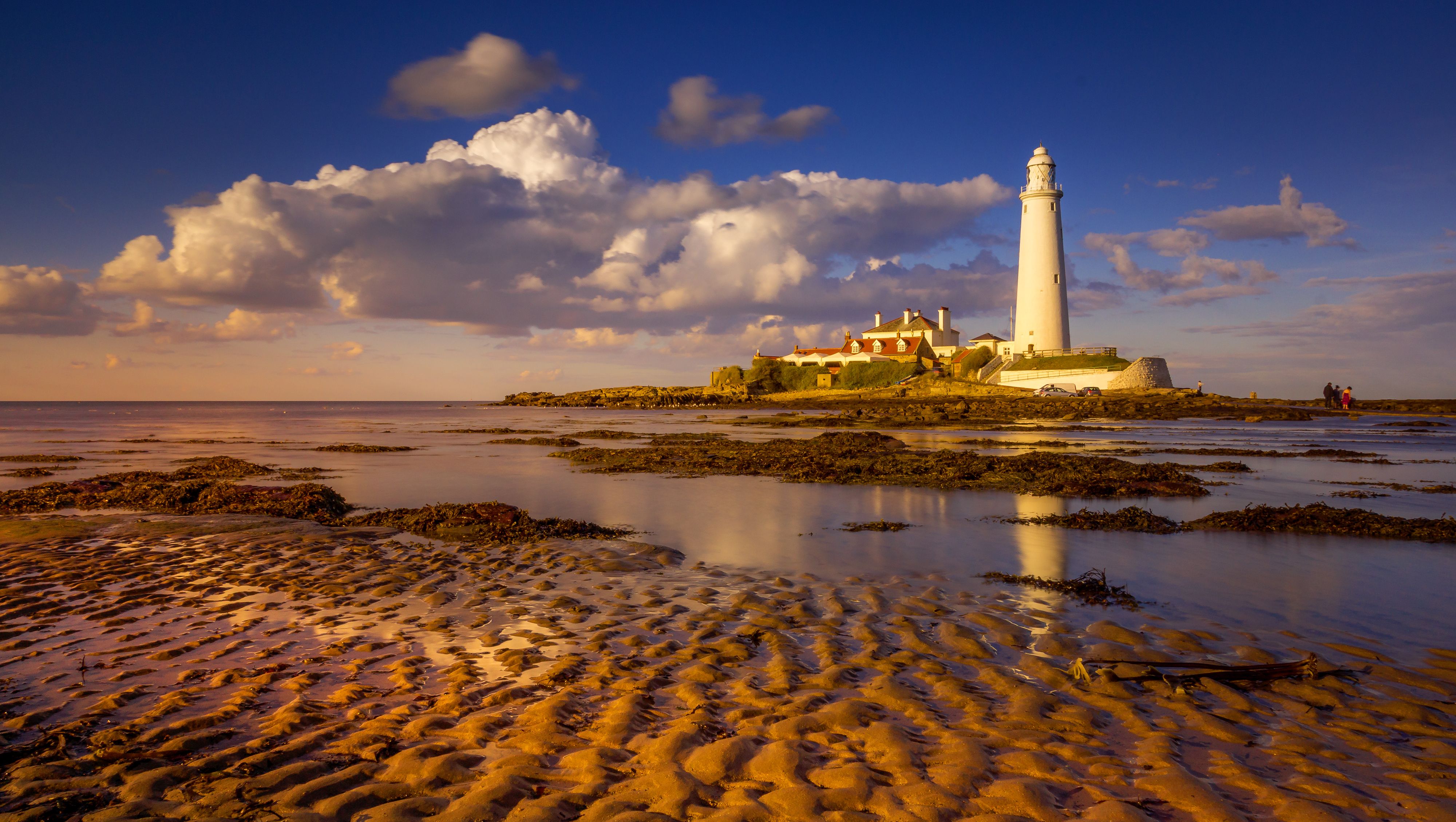 A lighthouse sits on the beach with sand and water · Free Stock Photo