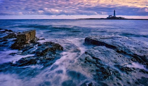 Free A beautiful seascape featuring St. Mary's Lighthouse with dramatic skies and waves at dusk. Stock Photo