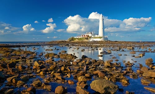 A lighthouse is seen on the rocks with water and clouds