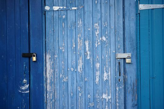 Weathered blue wooden doors with padlocks, showcasing rustic charm and security.