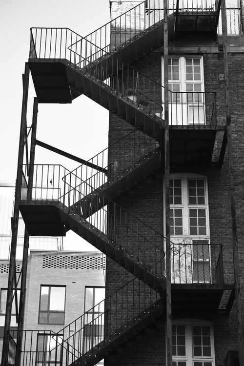 Free Black and white photo of a fire escape on a brick residential building in a city. Stock Photo