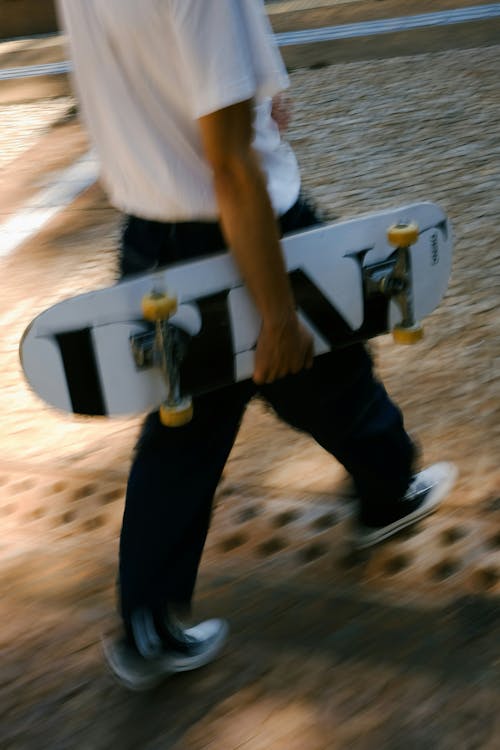 Man in White T-shirt Walking and Carrying Skateboard