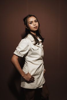 Elegant portrait of an Asian woman in a white dress, set against a brown studio background.