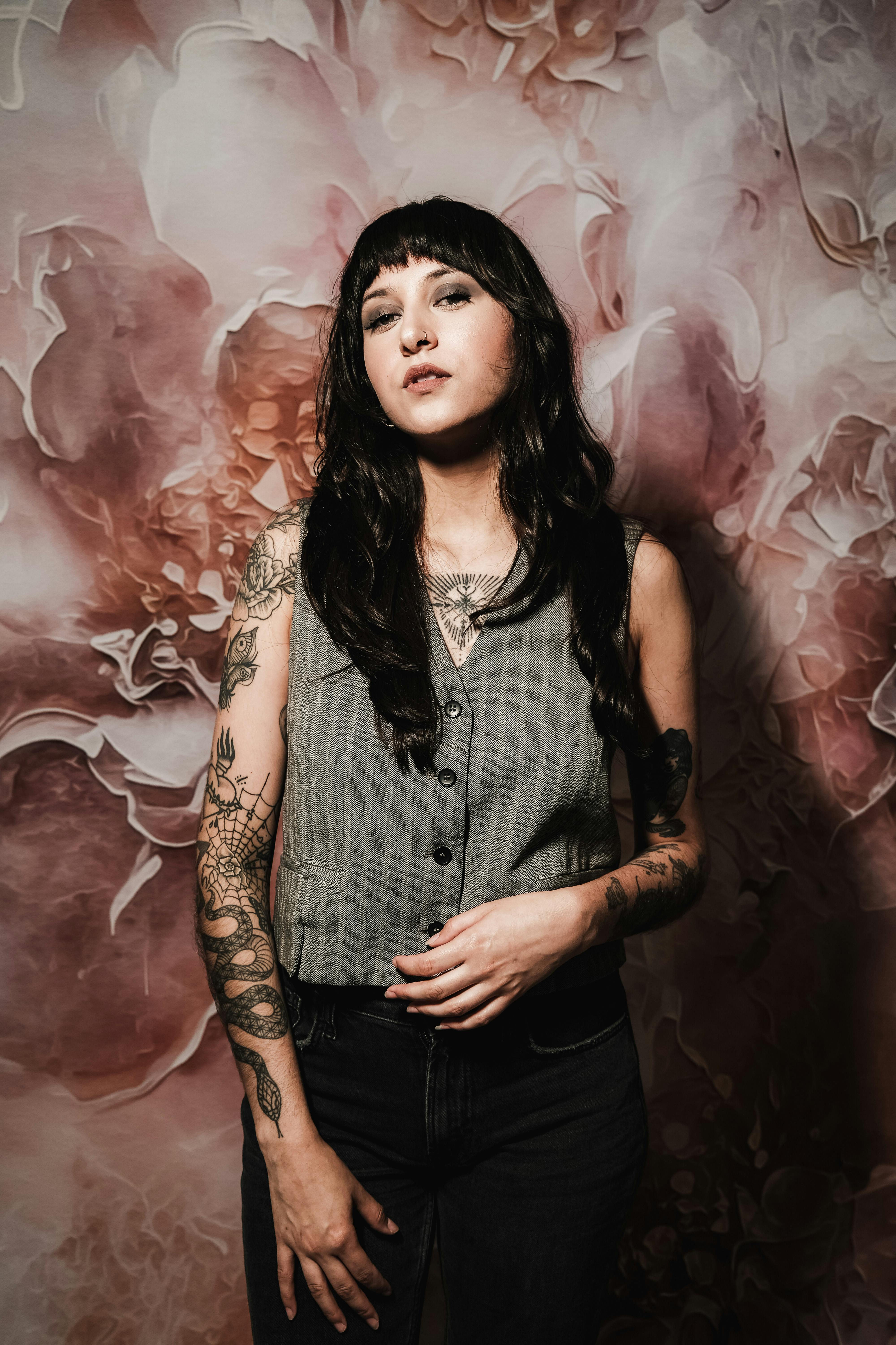 Tattooed woman standing in front of a floral backdrop, exuding contemporary fashion.