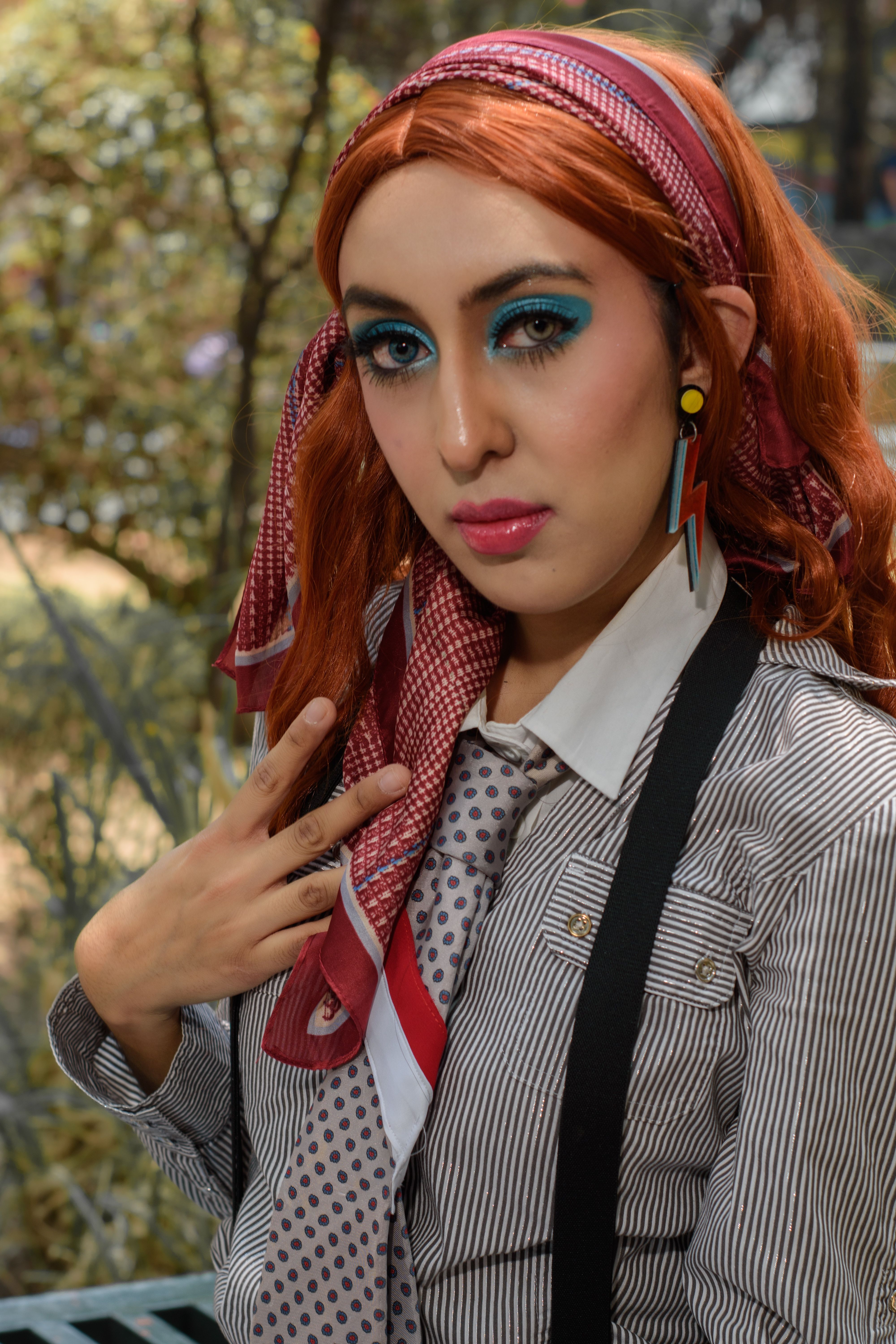 Stylish redhead woman with blue makeup and necktie posing in outdoor setting, Ciudad de México.