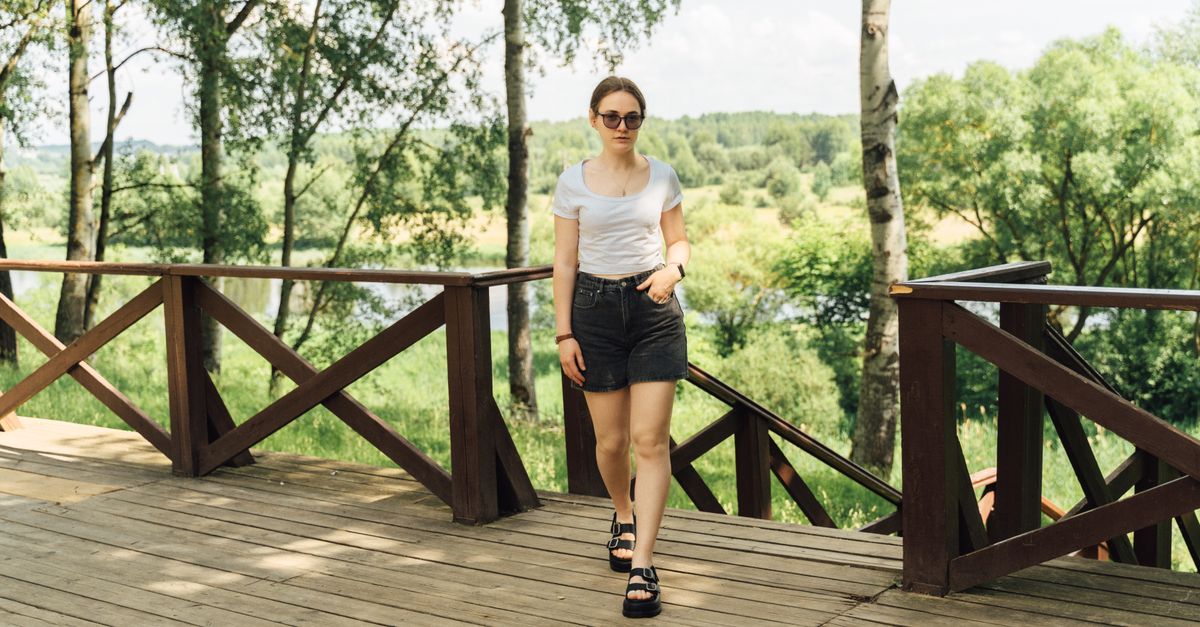 Casual summer fashion portrait of a woman walking on a wooden deck surrounded by lush greenery.