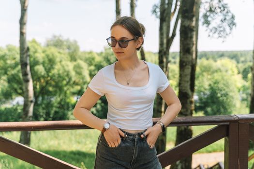 Casual outdoor portrait of a young woman wearing sunglasses and a white t-shirt, enjoying a sunny day in nature.
