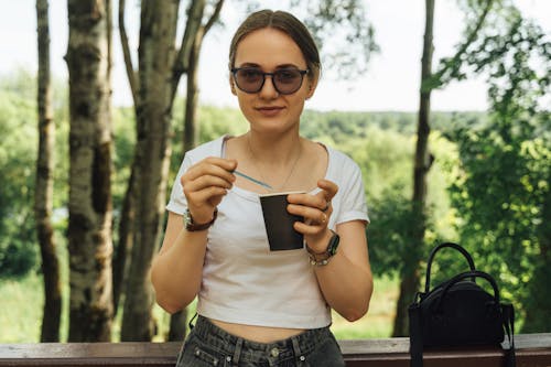 A woman in sunglasses eating a cup of coffee