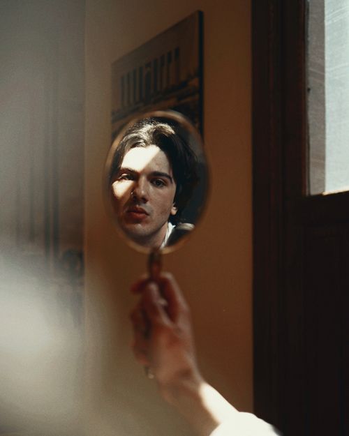 Free Artistic image of a young man reflected in a handheld mirror indoors. Stock Photo
