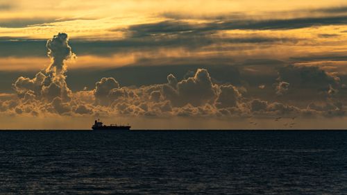 Free A tranquil scene with a cargo ship on the horizon during a vibrant sunset over the ocean. Stock Photo