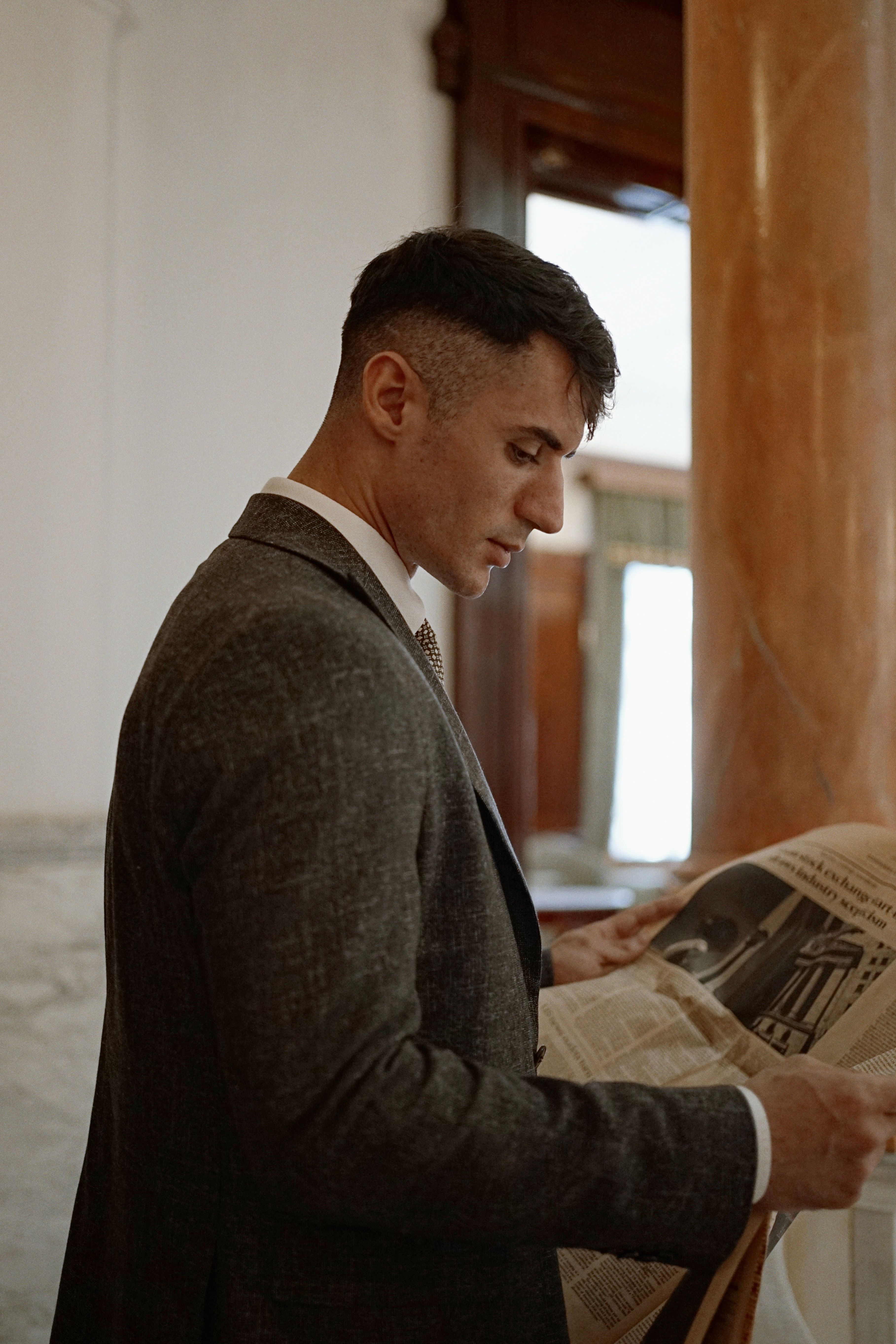 Side profile of a man in a suit reading a newspaper indoors, conveying sophistication.