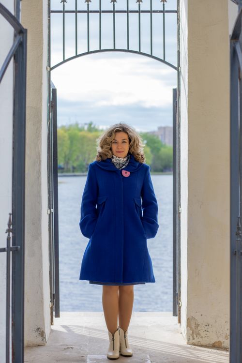 Free Stylish woman in a blue coat standing by an open gate overlooking a river. Stock Photo