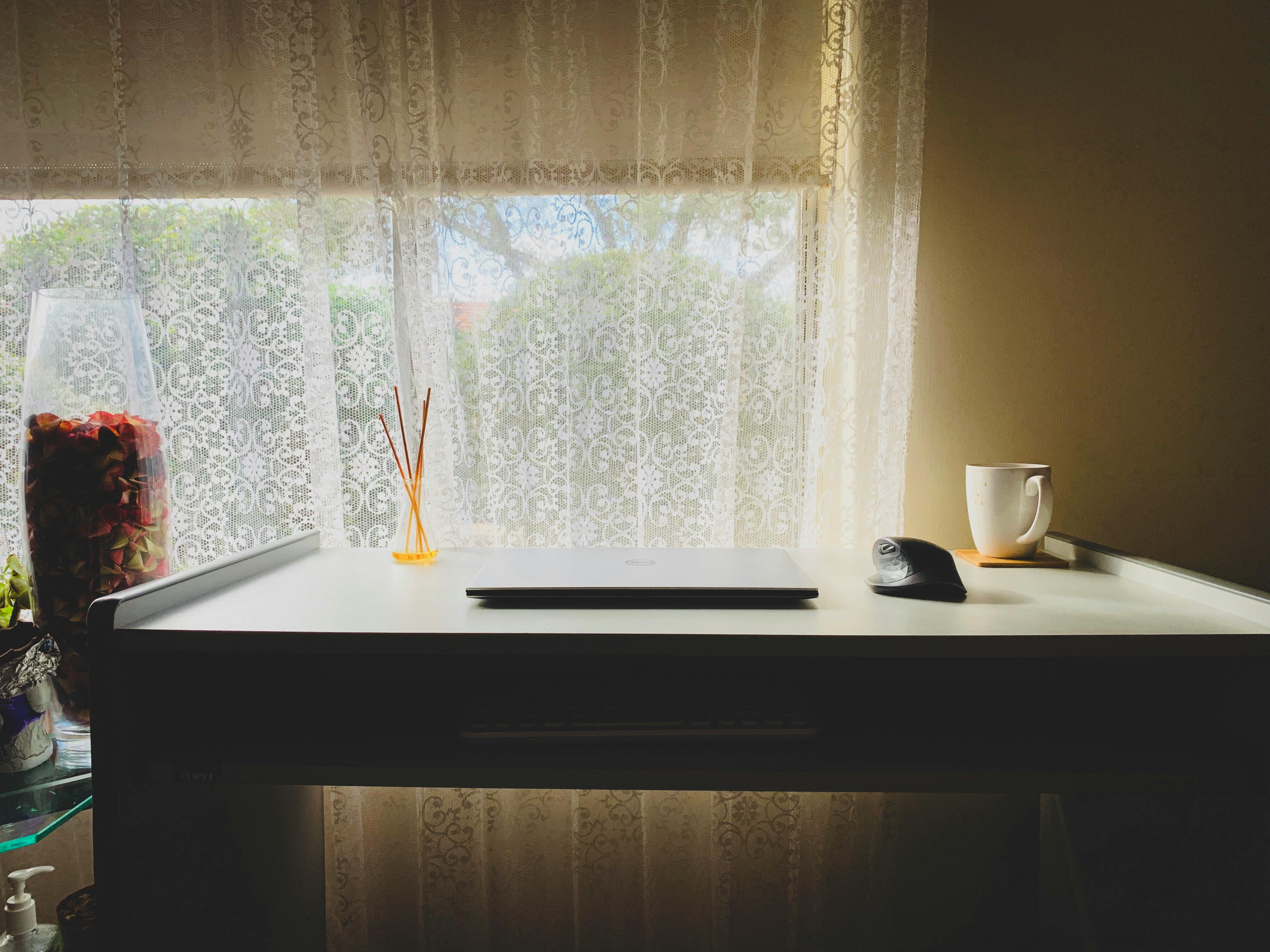 现代极简主义办公桌，配有笔记本电脑、鼠标和窗前的马克杯，是理想工作空间的灵感来源