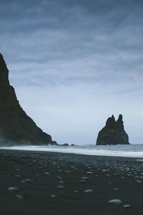 Free A dramatic view of Iceland's black sand beach near a striking sea stack and cliff. Stock Photo