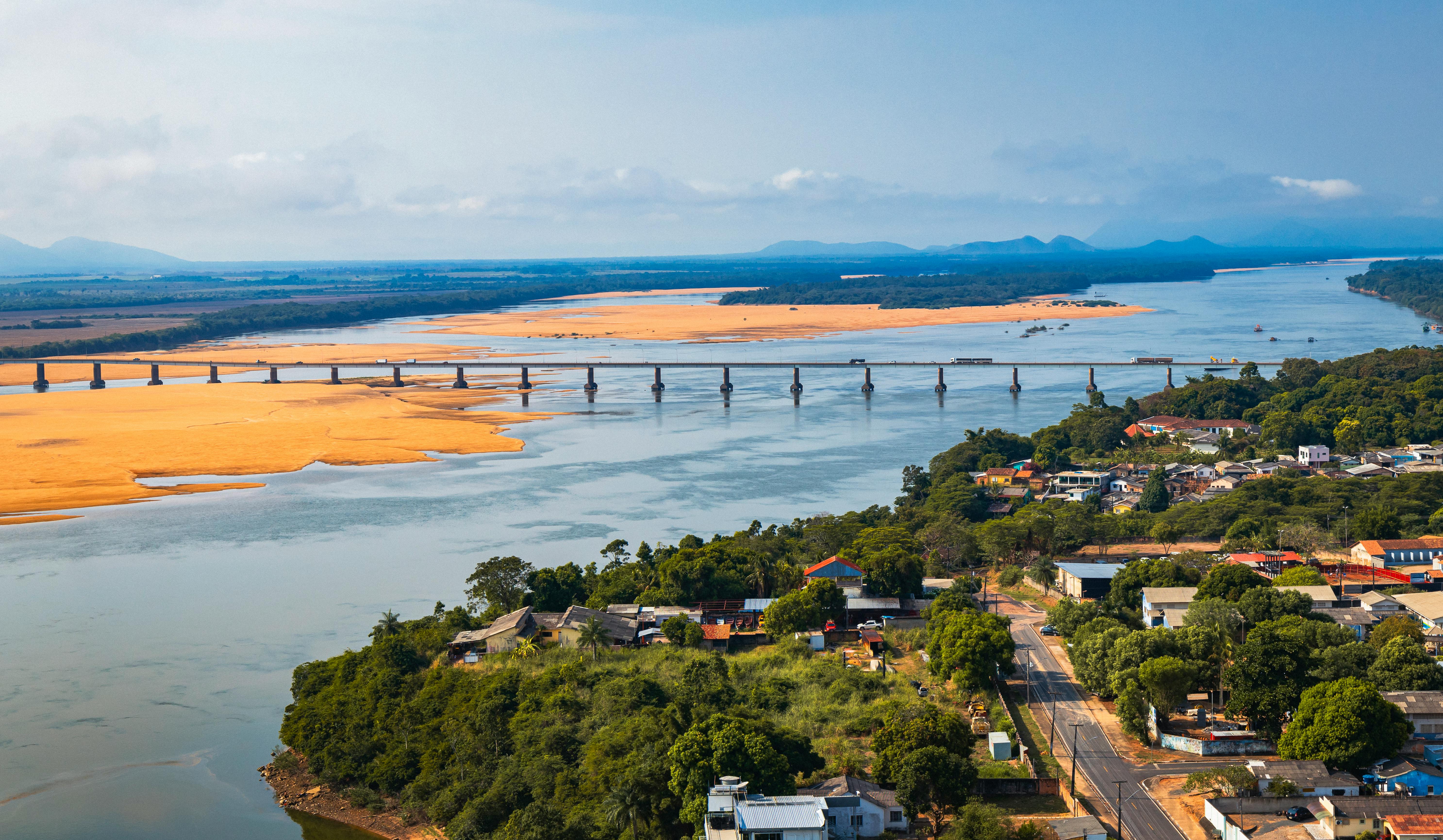 Scenic aerial view of a bridge crossing a river in Boa Vista, RR, with lush greenery and clear skies.