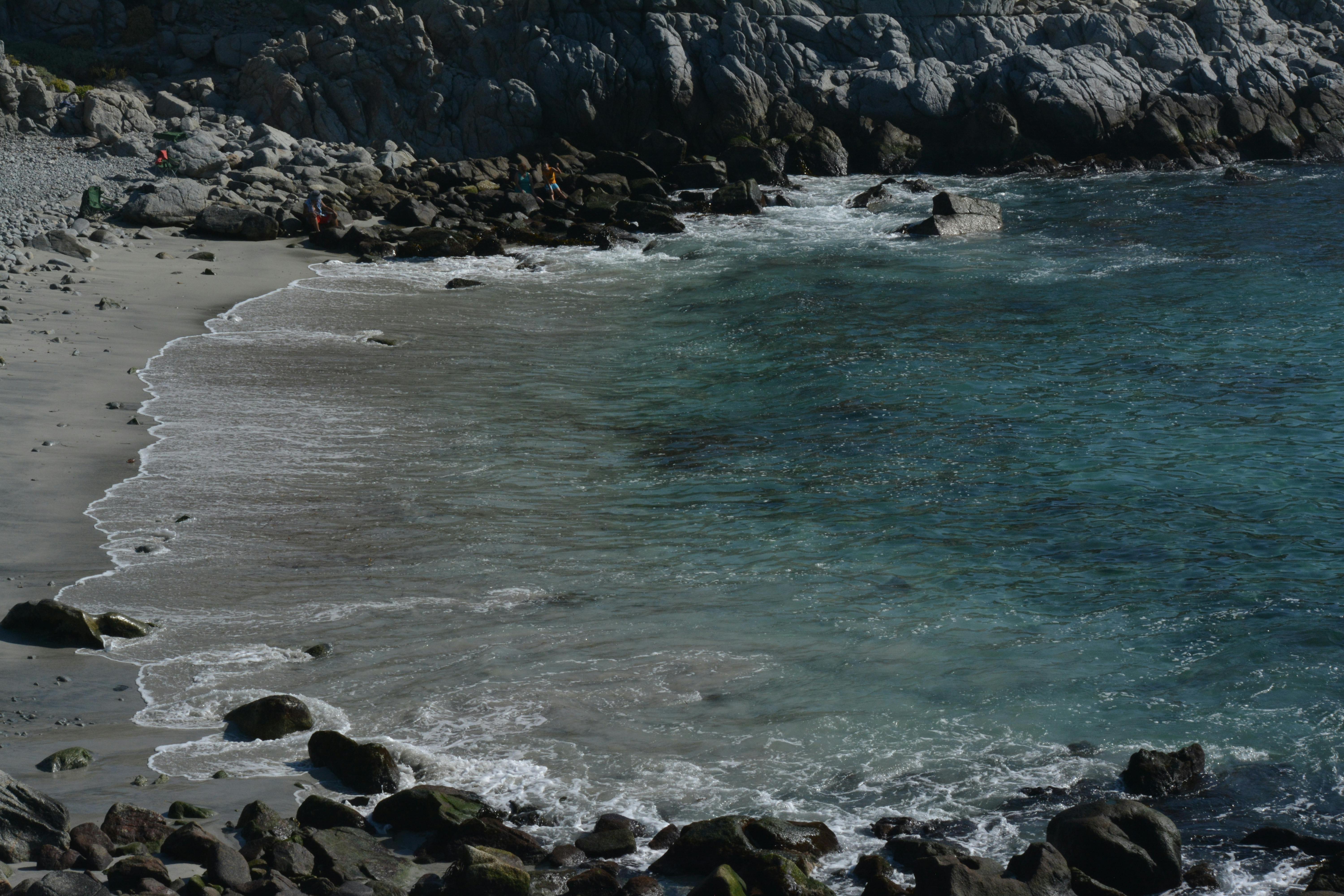 A tranquil coastal scene with crystal clear waters, sandy beach, and rugged cliffs under natural lighting.