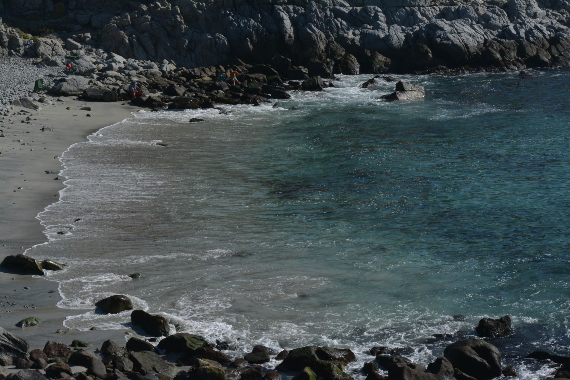 A tranquil coastal scene with crystal clear waters, sandy beach, and rugged cliffs under natural lighting.