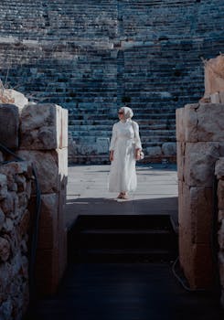 Woman in white dress and hijab stands in historic theatre in Kaş, Antalya.