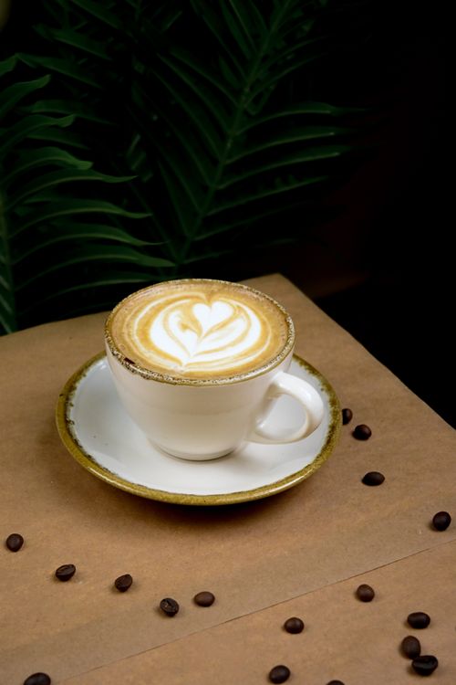 Free A beautiful cappuccino with heart-shaped latte art on a ceramic cup, surrounded by coffee beans and a cozy background. Stock Photo