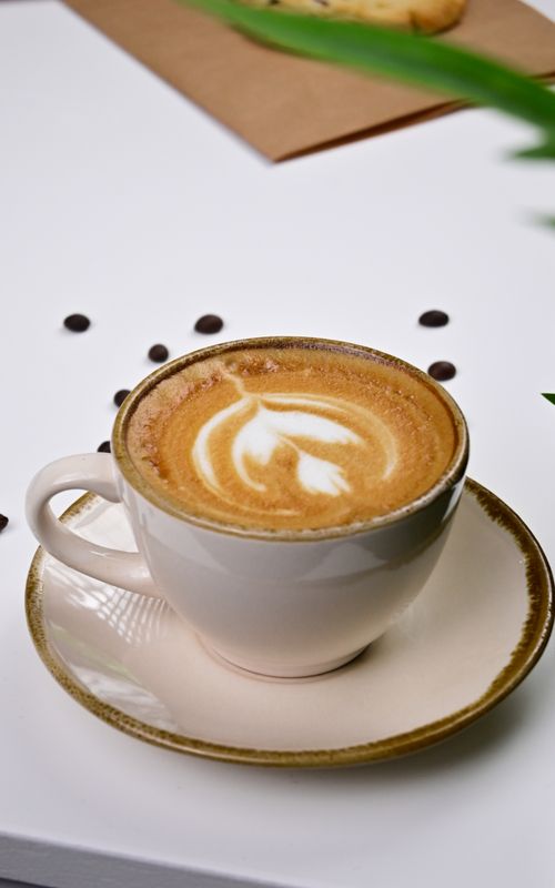 Free Close-up of a latte art cappuccino with coffee beans on a white table, creating a cozy coffee shop vibe. Stock Photo