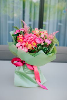 A stunning bouquet of mixed flowers wrapped in green paper with a red ribbon, placed on a table.