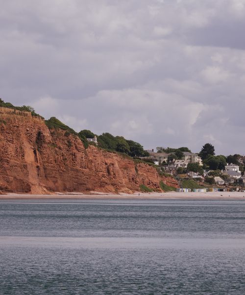 Free A picturesque view of red cliffs by the sea with charming seaside houses under a cloudy sky. Stock Photo