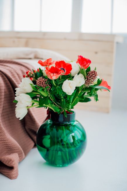 Beautiful flower arrangement with red and white flowers in a green glass vase on a cozy indoor setting.
