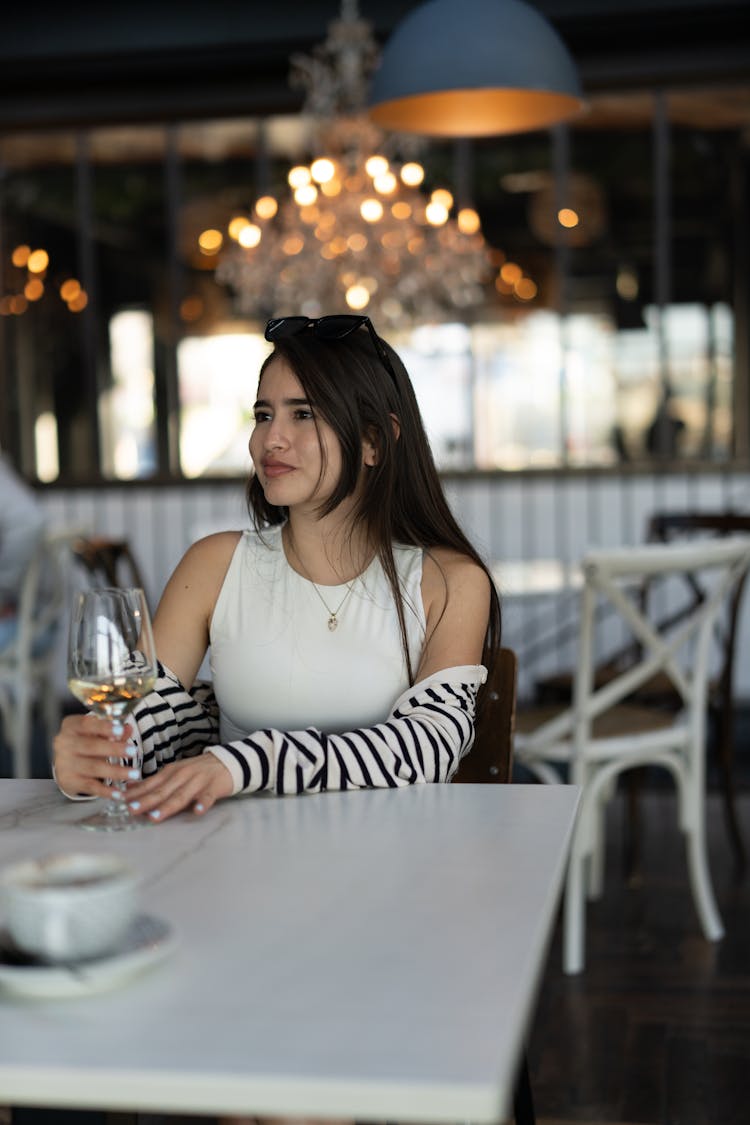 A Young Woman Sitting At A Table In A Restaurant With A Glass Of Wine 