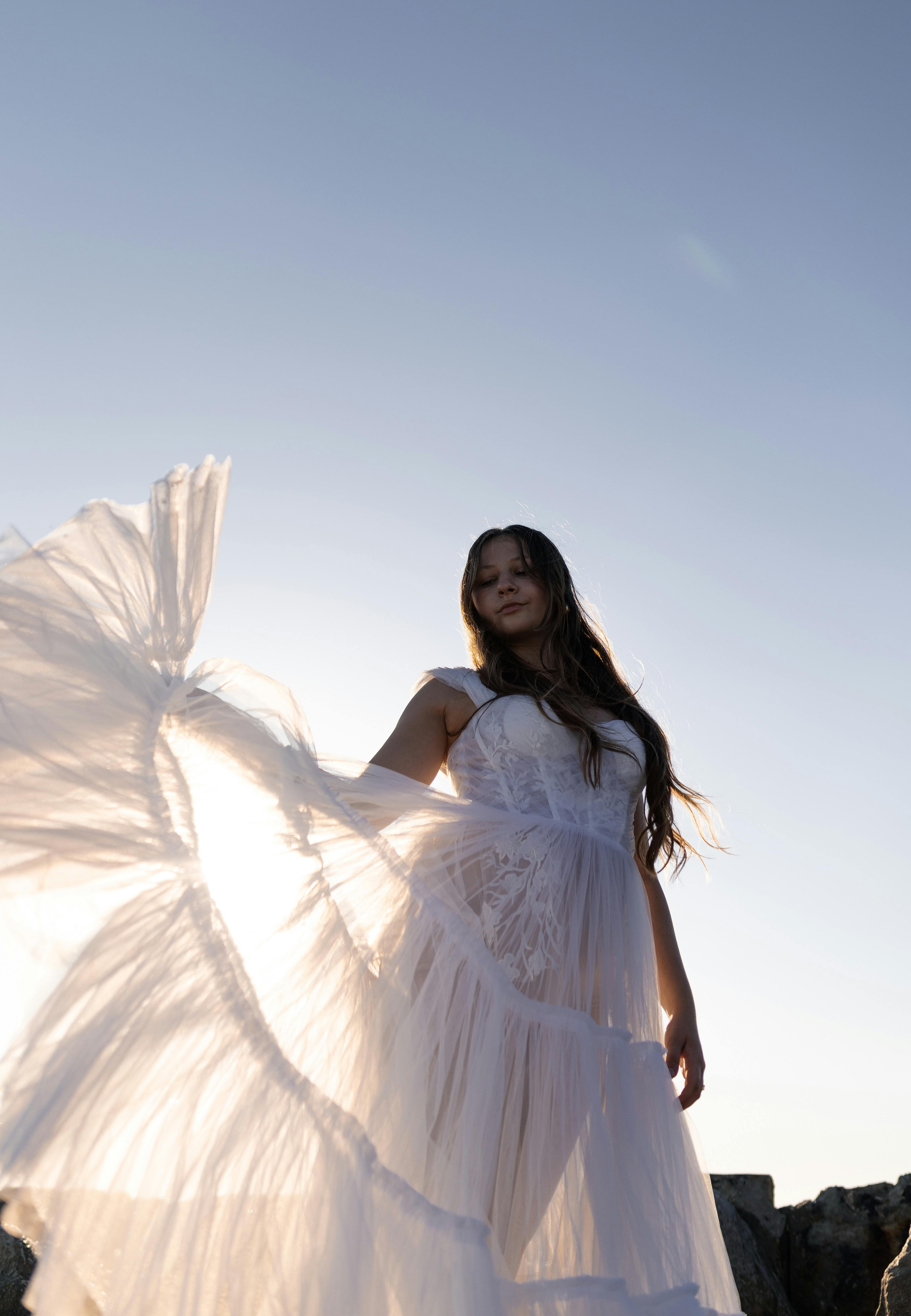 A woman gracefully poses in a flowing dress, backlit by the sunset for a dreamy effect.