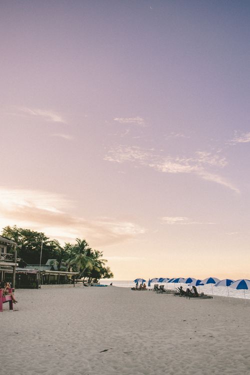Free Serene sandy beach with umbrellas and palm trees at sunset in Nadi, Fiji. Stock Photo