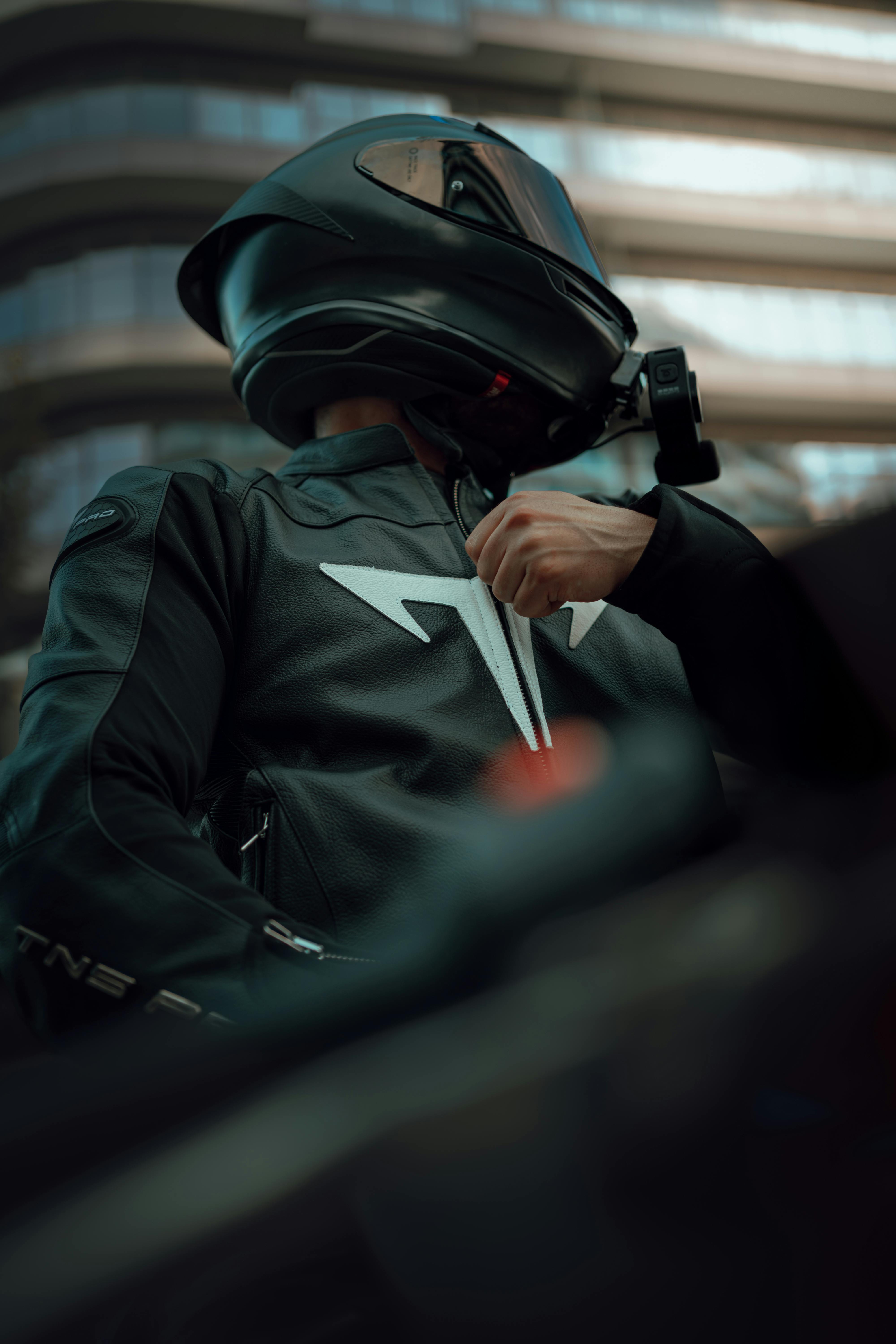 Motorcyclist in black attire adjusting jacket, low angle view in urban setting.