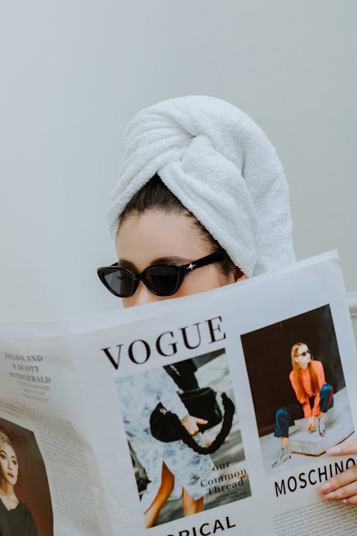A woman wearing a towel reading a vogue magazine