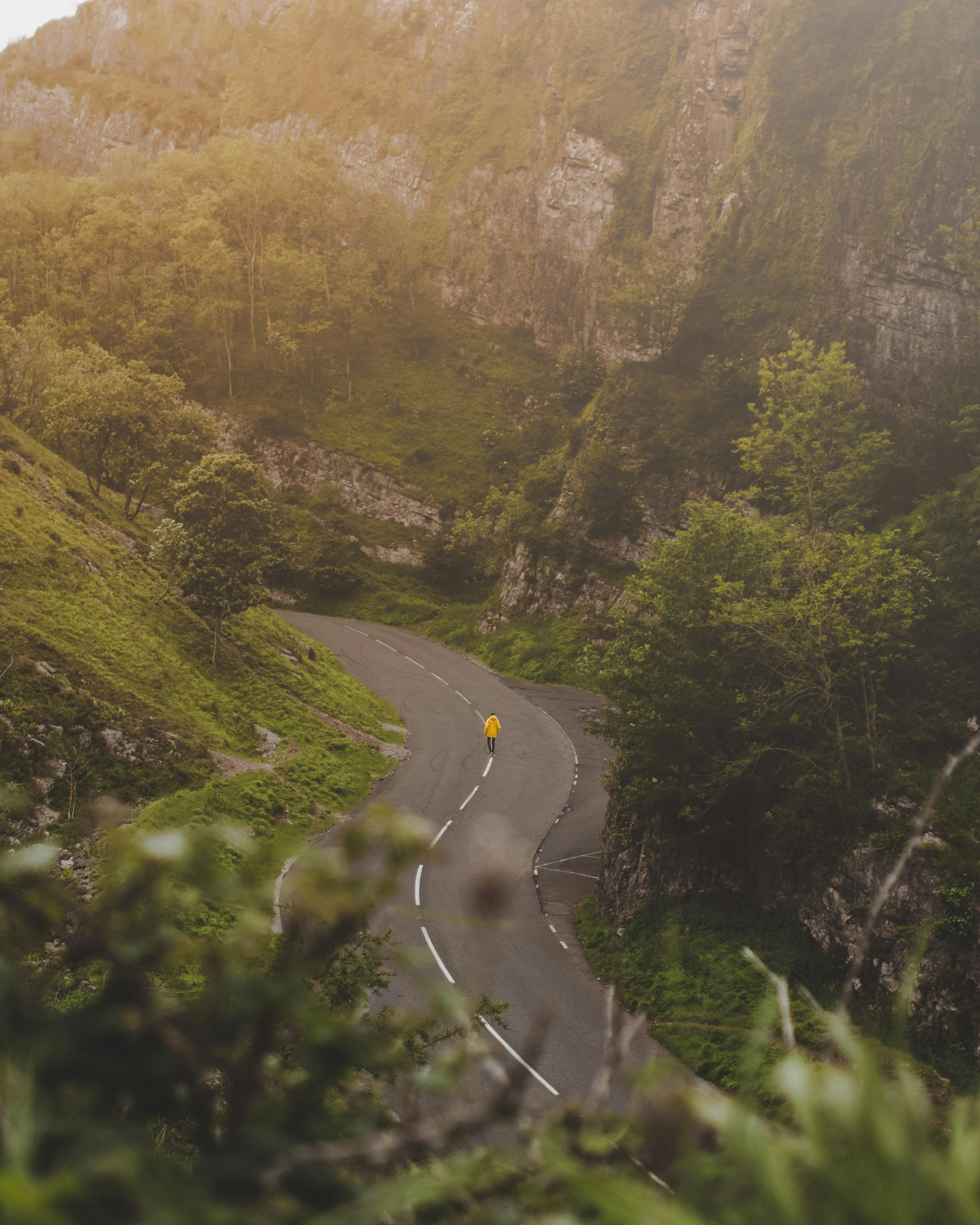 从空中俯瞰，一个骑自行车的人正穿行在蜿蜒于阳光普照、郁郁葱葱的山谷中的道路上