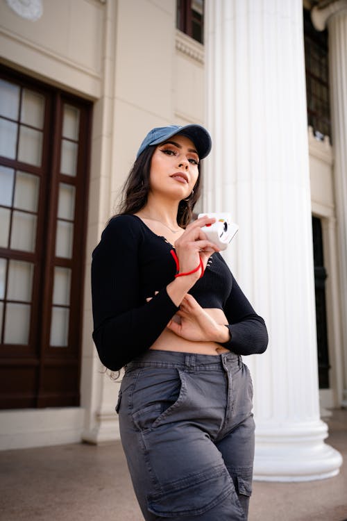 A woman in a cap and pants holding a cell phone
