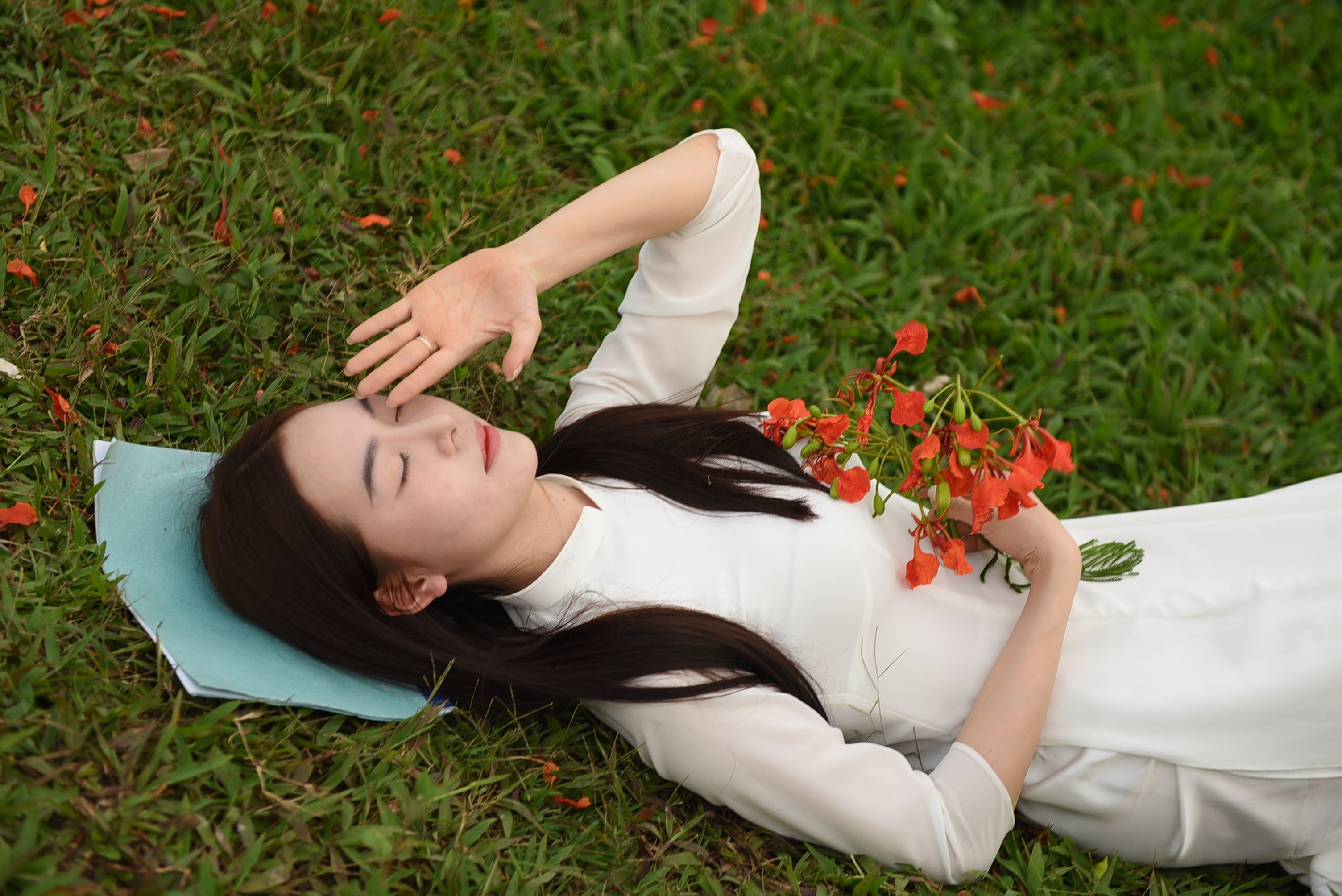 Woman in white dress lying on grass holding red flowers, serene and peaceful.