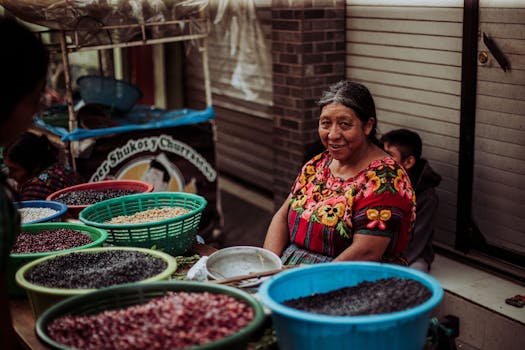 A cheerful woman in colorful attire selling various beans at an outdoor market.