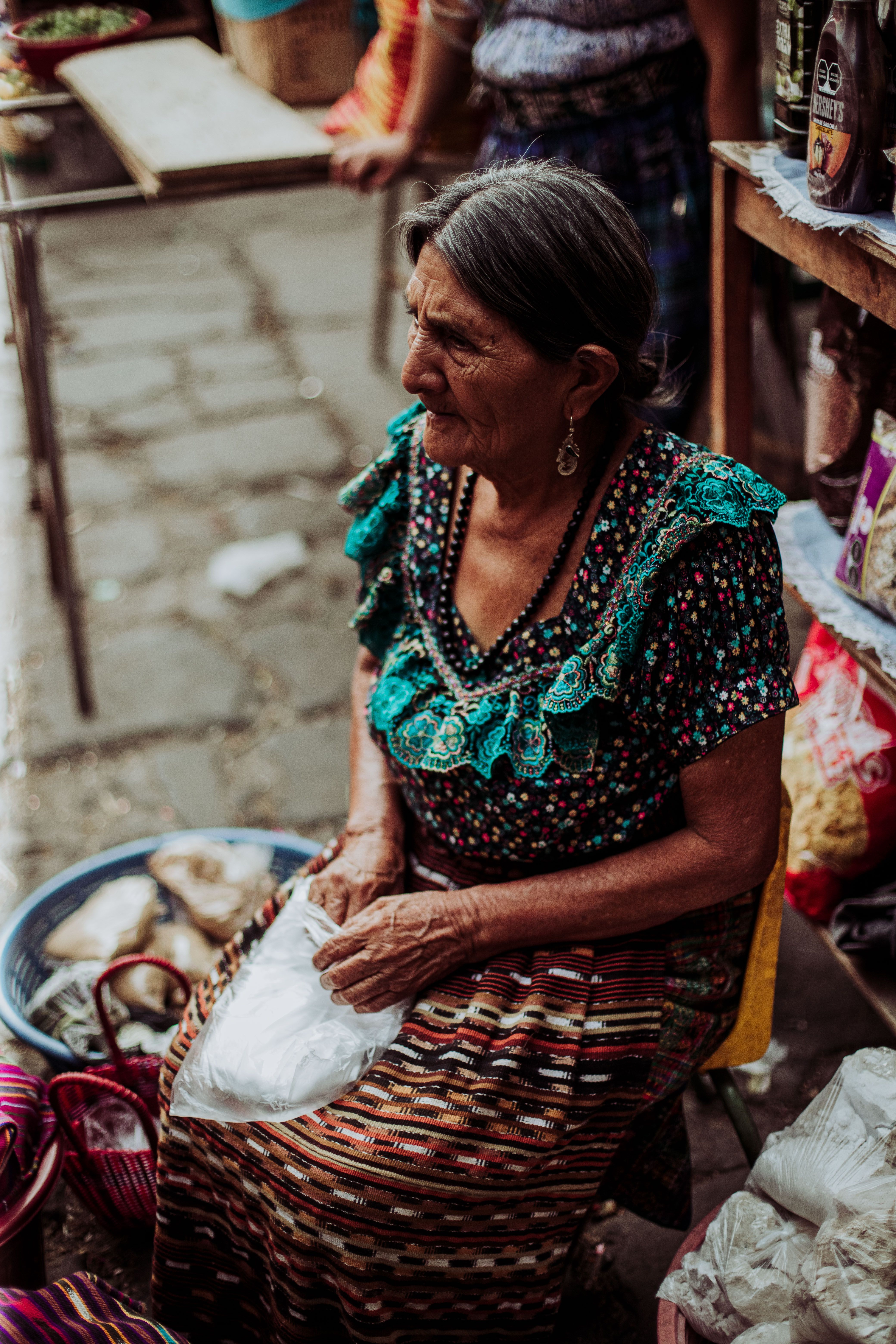 Senior woman in traditional attire selling products at a vibrant outdoor market.