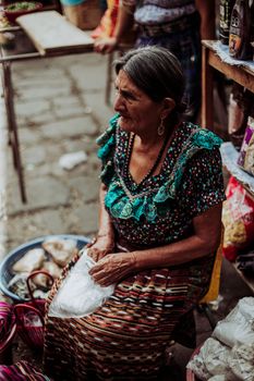 Senior woman in traditional attire selling products at a vibrant outdoor market.