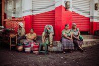 Elderly vendors sitting by a store, selling goods in an urban street setting.
