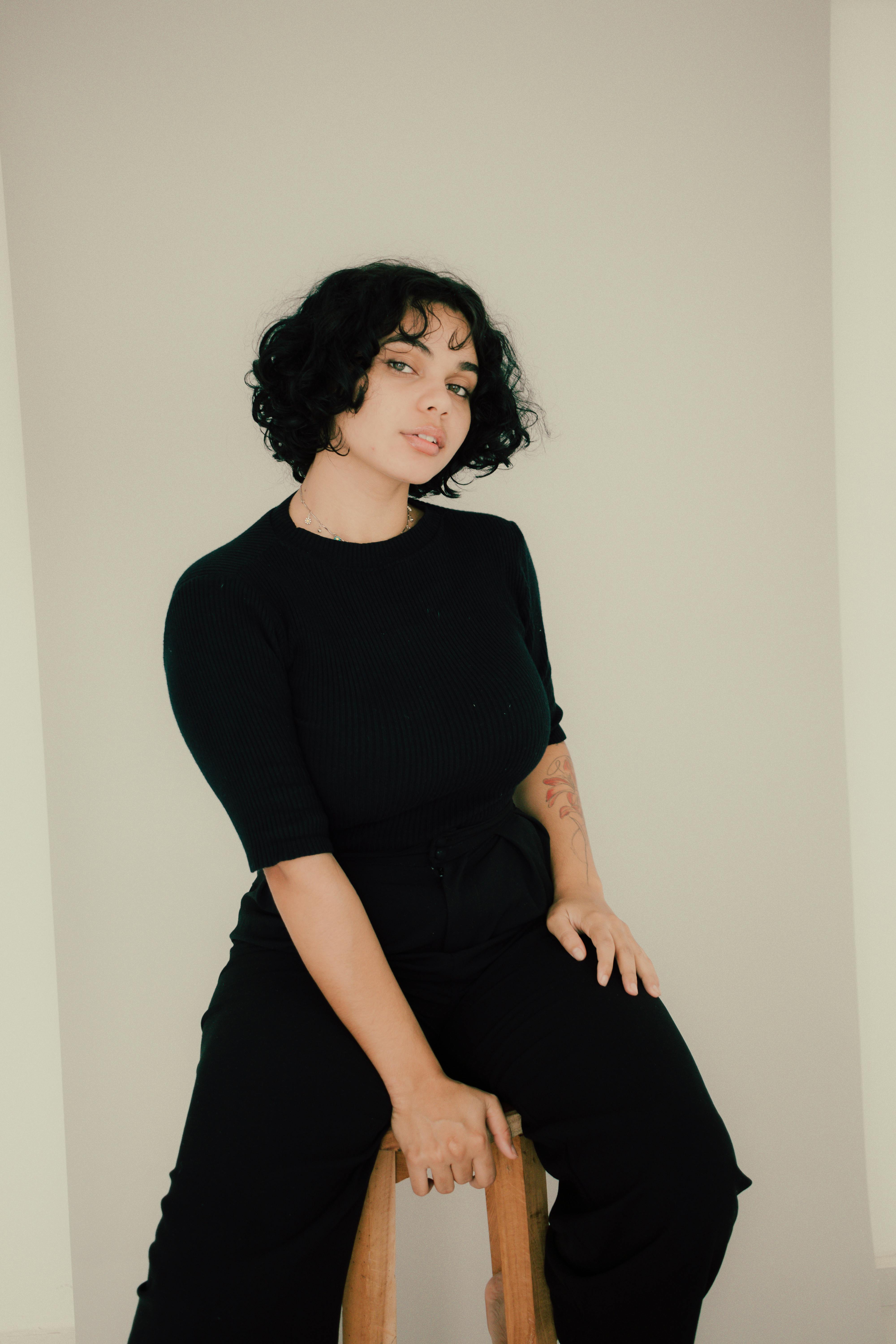 Elegant portrait of a young woman sitting on a stool, wearing casual black attire