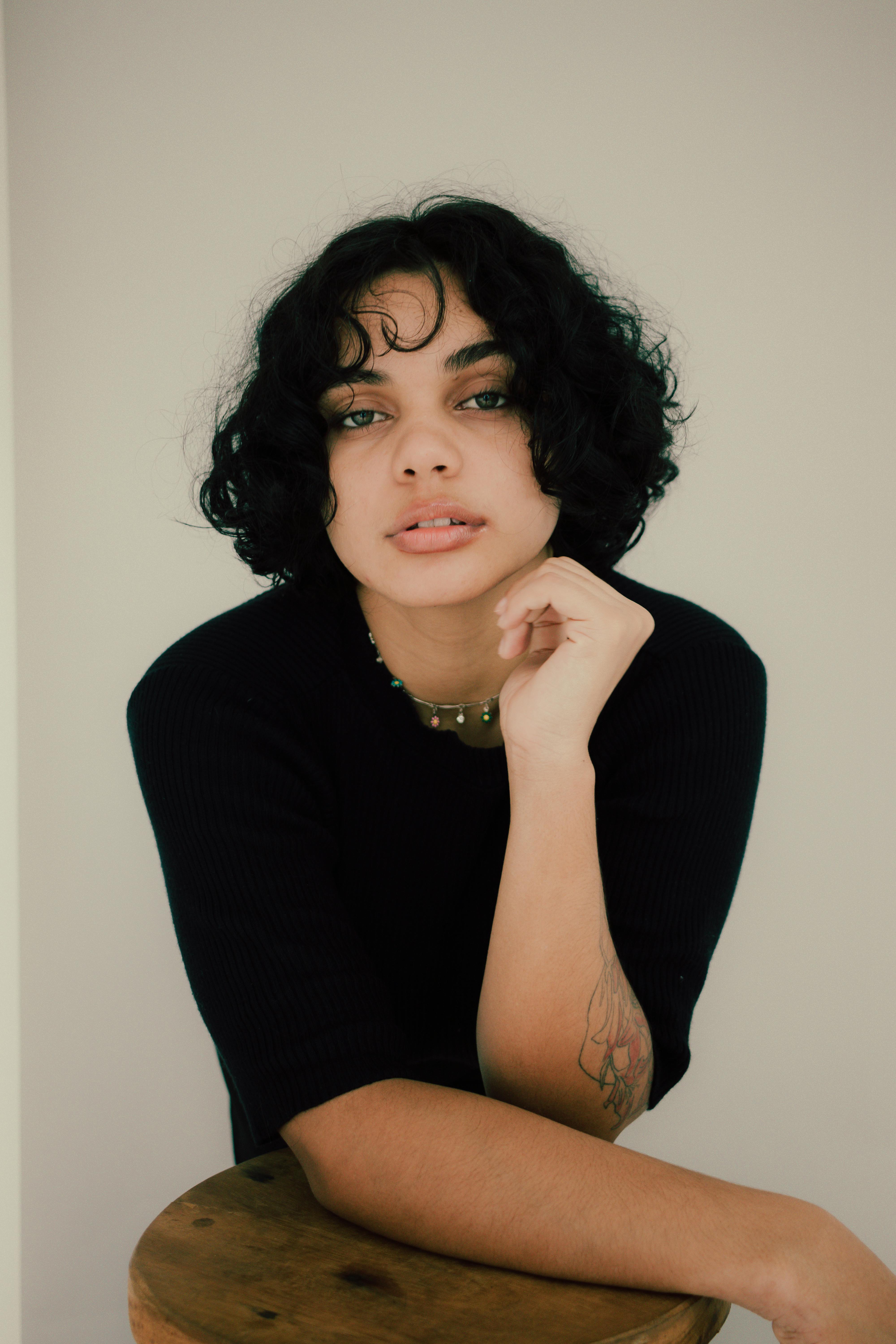 Stylish portrait of a young brunette woman in a black t-shirt against a white background.