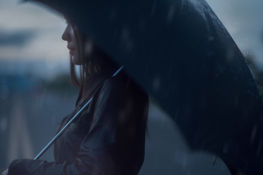 Profile of a woman holding an umbrella in the rain, evoking a moody and introspective atmosphere.