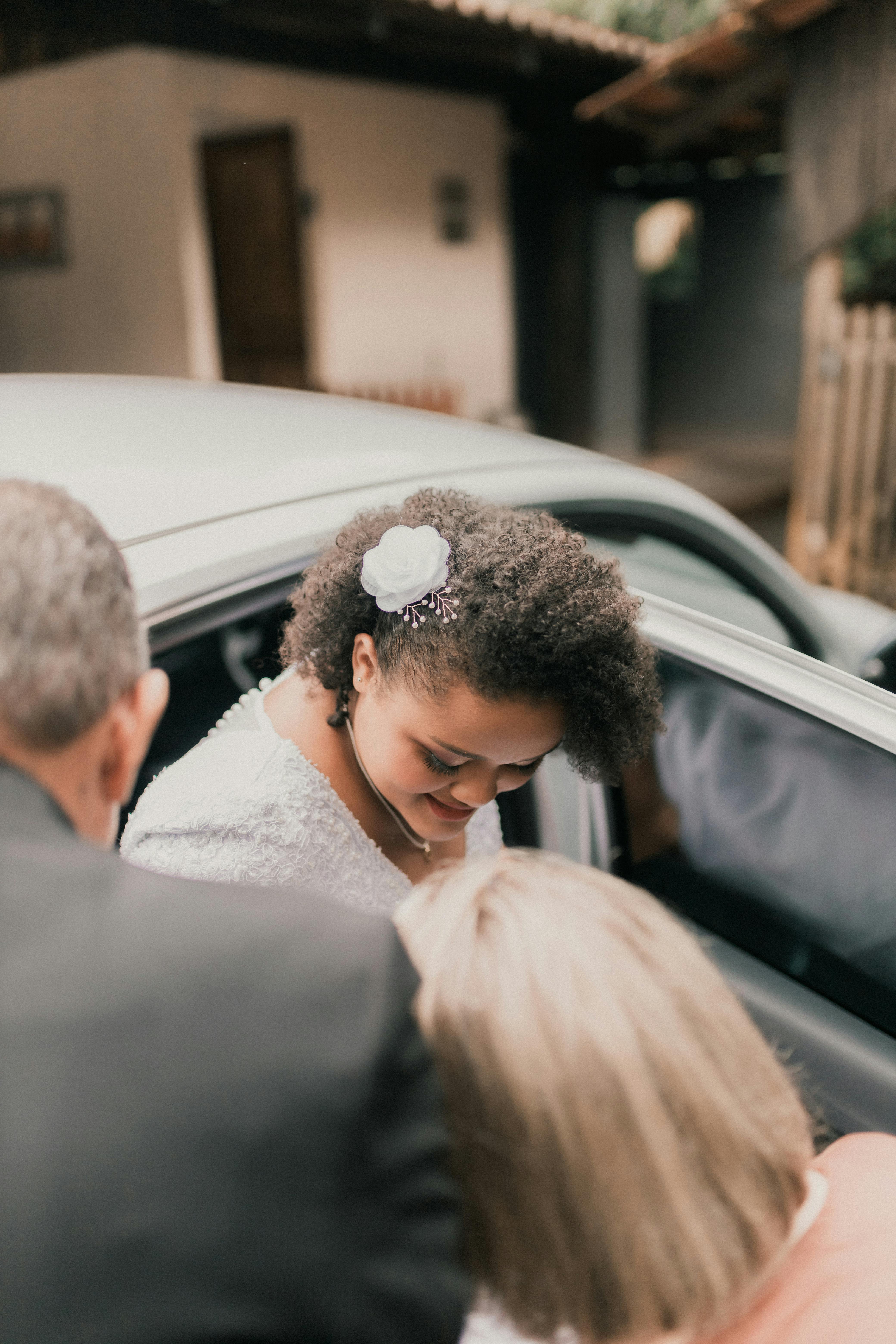 A beautiful bride steps into a car, surrounded by loved ones, capturing a candid wedding moment.