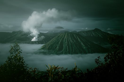 A dramatic landscape of Mount Bromo with fog and volcanic smoke captured at sunrise in Indonesia.