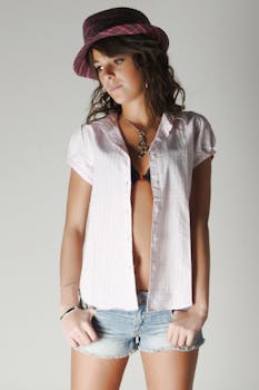 Young woman posing in casual attire with hat and open shirt against a studio backdrop.