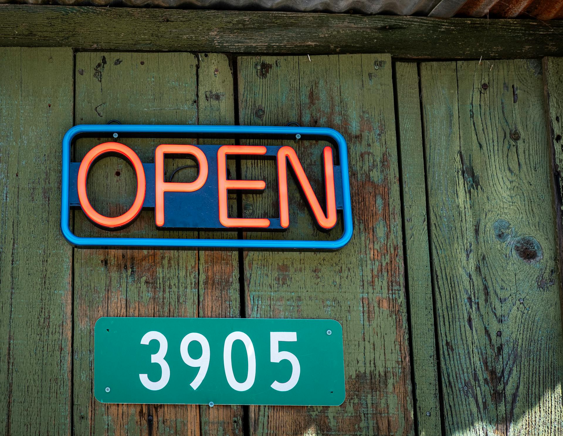 Close-up of a red neon open sign and address on rustic wooden wall.